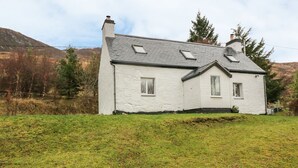 A white house with a sloped roof, two chimneys, and a small front porch. - Creag Mhor Cottage (Kyle)