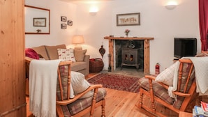A cozy living room with a fireplace, wooden furniture, and a television. - Creag Mhor Cottage (Kyle)