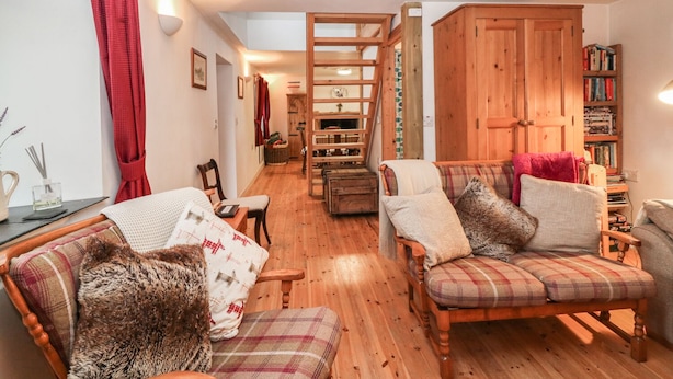 A cozy living room with wooden flooring, a fireplace, a wooden cabinet, and a bookshelf. - Creag Mhor Cottage (Kyle)