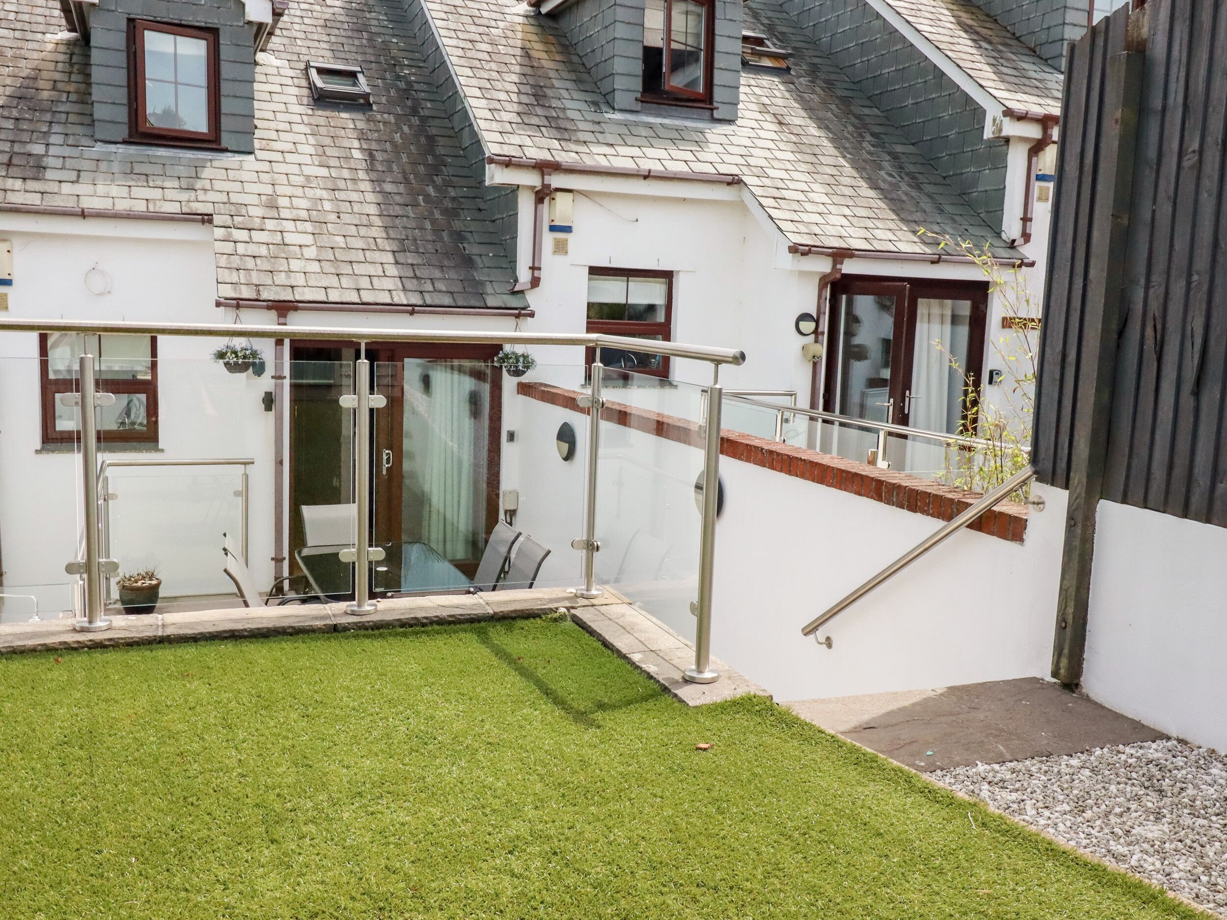 A residential building with a small garden, a glass door entrance, and a staircase leading to a balcony.