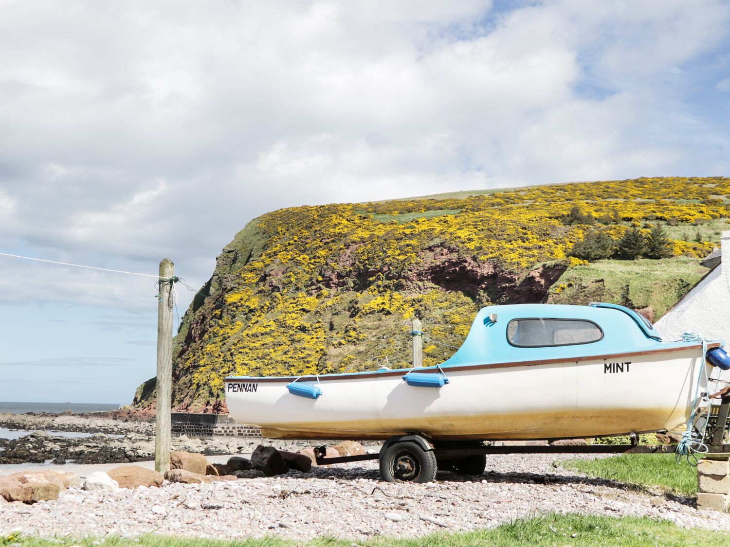 A boat named PENNAN on a trailer near a rocky shore with a cliff in the background.