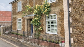 A stone building with a brick facade, white window shutters, and a metal fence. - Bertelle (King's Lynn)