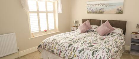 Quarto com cama grande, janela com cortinas, radiador e um quadro na parede.