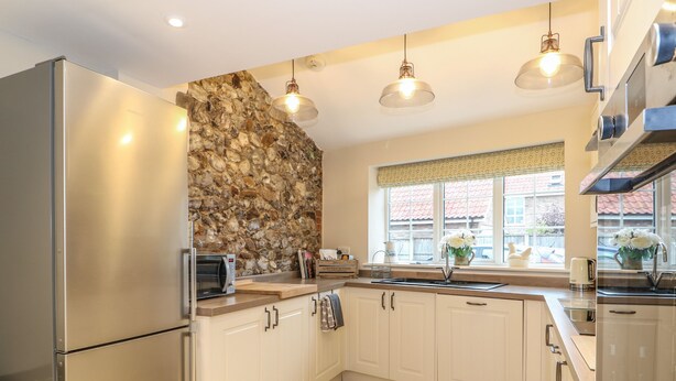A modern kitchen with a stone backsplash, stainless steel appliances, and a window with a view of the outside. - Bertelle (King's Lynn)