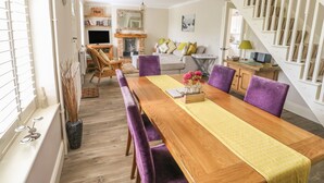 A dining area with a wooden table, purple chairs, and a yellow table runner. There is a fireplace, a sofa, and a staircase in the background. - Bertelle (King's Lynn)