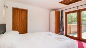 A bedroom with a bed, a wooden wardrobe, a door, and a window with a view of the outside. - The Stone Barn (Shepton Mallet)