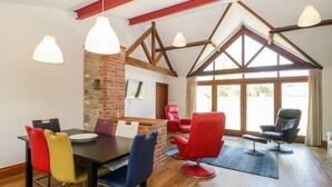 A dining area with a brick wall, wooden beams, and a large window. - The Stone Barn (Shepton Mallet)