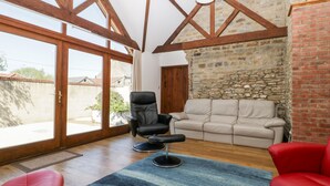 A spacious living room with a stone wall, a wooden ceiling, and a large sliding glass door leading to an outdoor area. - The Stone Barn (Shepton Mallet)