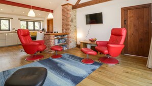 A modern living room with red leather chairs, a black ottoman, and a blue patterned rug. - The Stone Barn (Shepton Mallet)