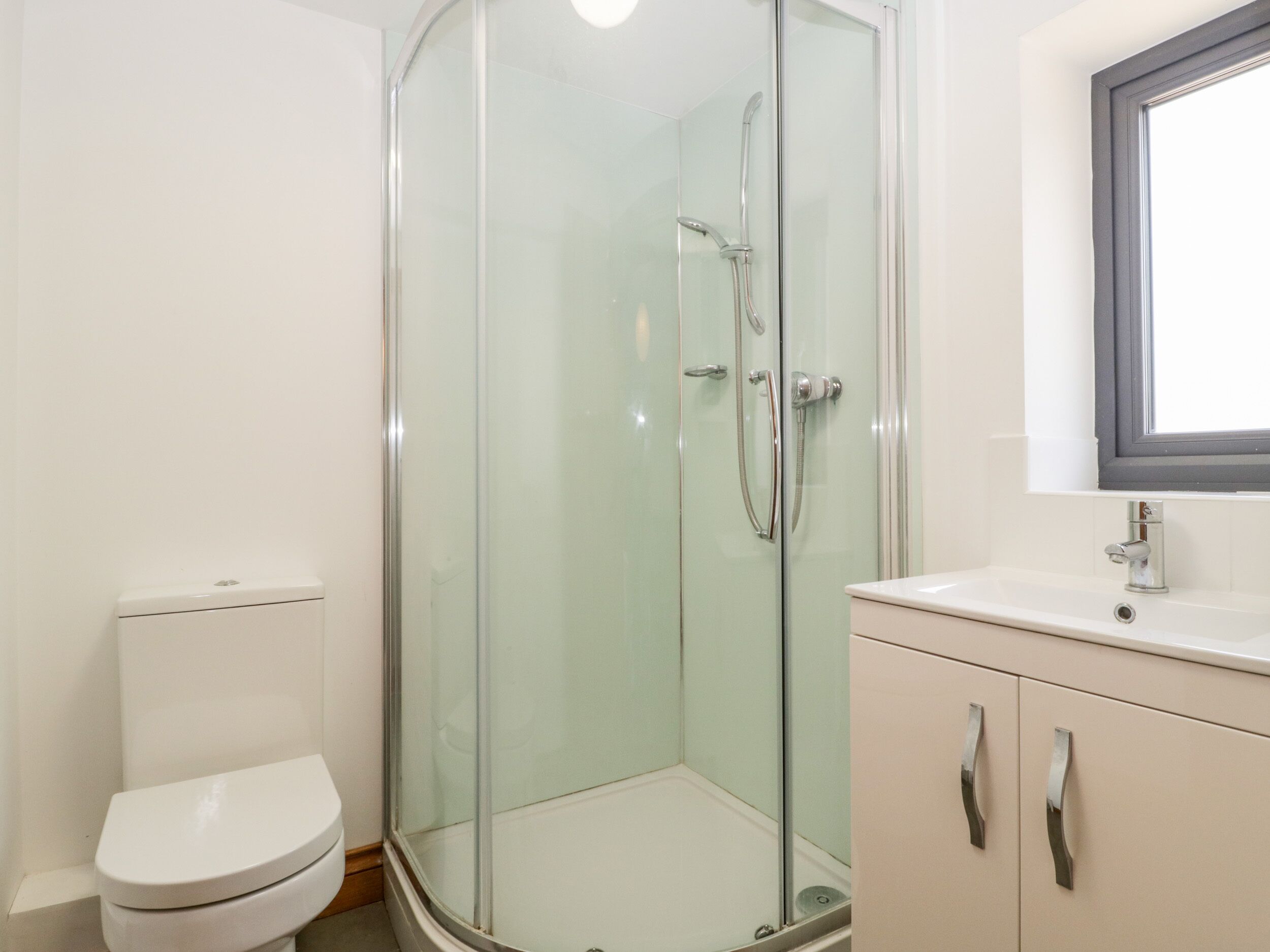 A modern bathroom with a glass-enclosed shower, a toilet, and a vanity with cabinets.
