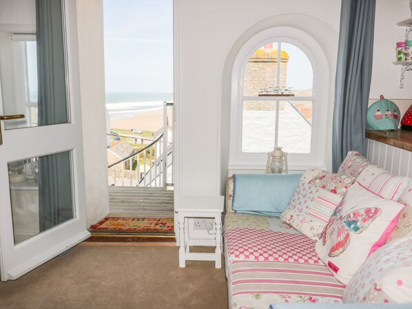 A cozy room with a view of the beach, a small table with a lamp, and a colorful sofa. - Spiral View (Perranporth)