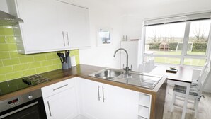 A modern kitchen with white cabinets, a stainless steel sink, and a built-in oven. - Driftwood (Bude)