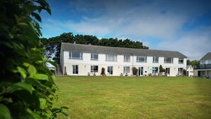 A two-story residential building with a large front lawn, multiple windows, and outdoor seating areas. - Driftwood (Bude)