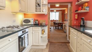 Una cocina con armarios blancos, estufa a gas, microondas y comedor con mesa y sillas.