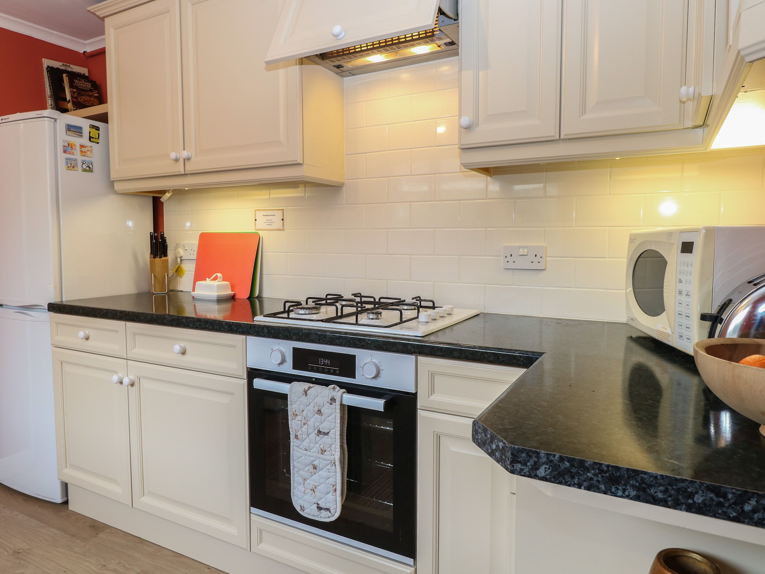 Una cocina con gabinetes blancos, estufa a gas, horno, microondas y refrigerador.