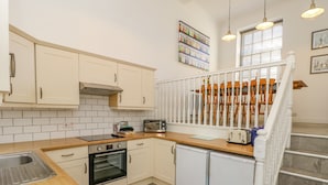 A modern kitchen with white cabinets, a wooden countertop, a built-in oven, a refrigerator, and a dining area visible through a white fence.