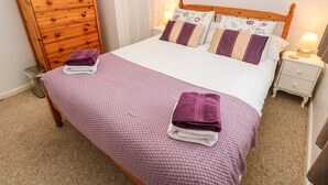Una cama bien hecha con una manta rosa con textura, dos almohadas con motivos florales y dos toallas dobladas sobre la cama.