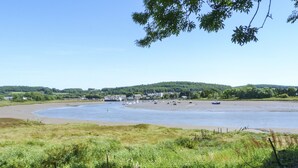 Un paysage côtier avec une plage de sable, des bateaux et une colline boisée en arrière-plan.