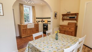 Une cuisine chaleureuse avec des meubles en bois, une table blanche recouverte d’une nappe à motifs floraux et un vase rempli de fleurs.