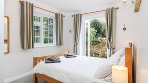 Een slaapkamer met een houten bed, wit beddengoed, een bedlampje en gordijnen.