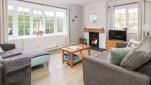 Een knusse woonkamer met een open haard, comfortabele zithoek en grote ramen.