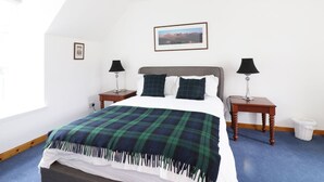 A bedroom with a bed, two nightstands, a lamp on each, a framed picture on the wall, and a window. - Dunnottar Woods House (Stonehaven)