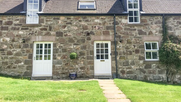 A stone building with two white doors, a small window, and a chimney. - Dunnottar Woods House (Stonehaven)
