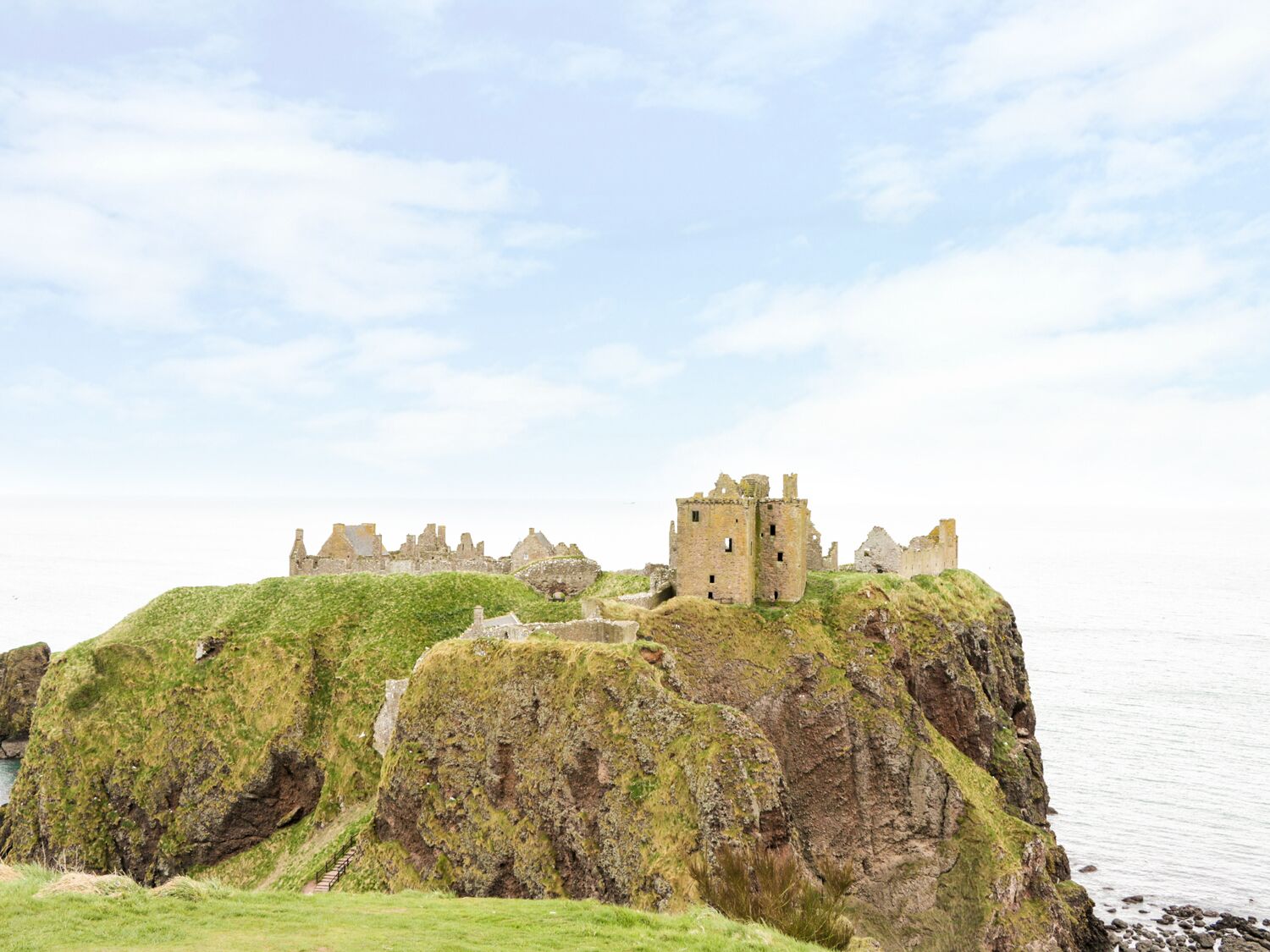 A historic castle ruin on a grassy cliff by the sea.