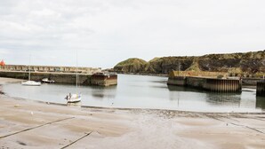 A coastal scene with a sandy beach, a pier, and a boat docked near the shore. - Dunnottar Woods House (Stonehaven)