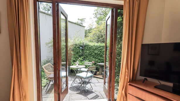 A room with a sliding glass door leading to an outdoor patio with a table and chairs. - Doe Foot Cottage (Carnforth)