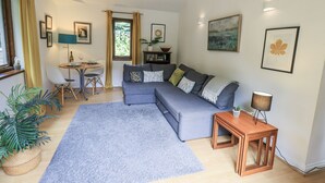 A living room with a grey sofa, a small wooden table, a blue rug, and a window with curtains. - Doe Foot Cottage (Carnforth)