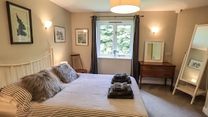 A bedroom with a bed, a dresser, a chair, a mirror, and framed pictures on the wall. - Doe Foot Cottage (Carnforth)