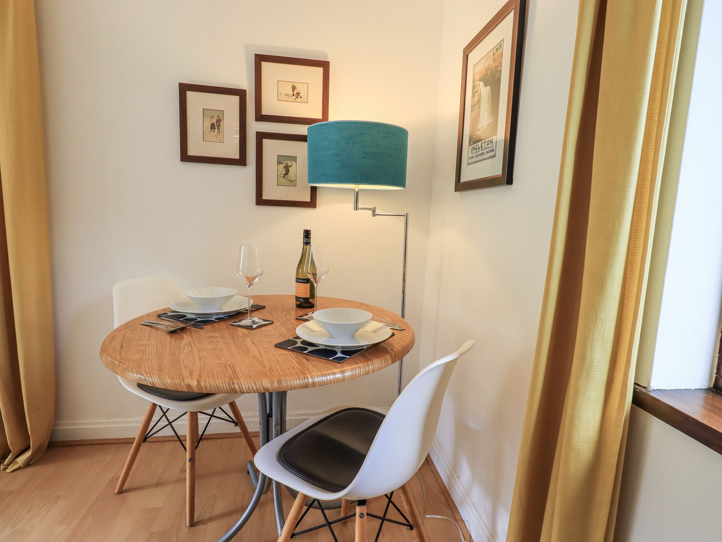 A round dining table with two chairs, a bottle of wine, and a teal floor lamp.