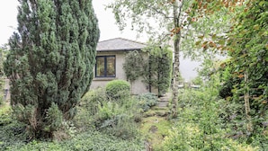 A house surrounded by dense greenery, including tall trees and shrubs. - Doe Foot Cottage (Carnforth)