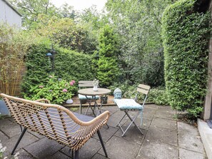 A patio with wicker furniture, a Buddha statue, and lush greenery. - Doe Foot Cottage (Carnforth)
