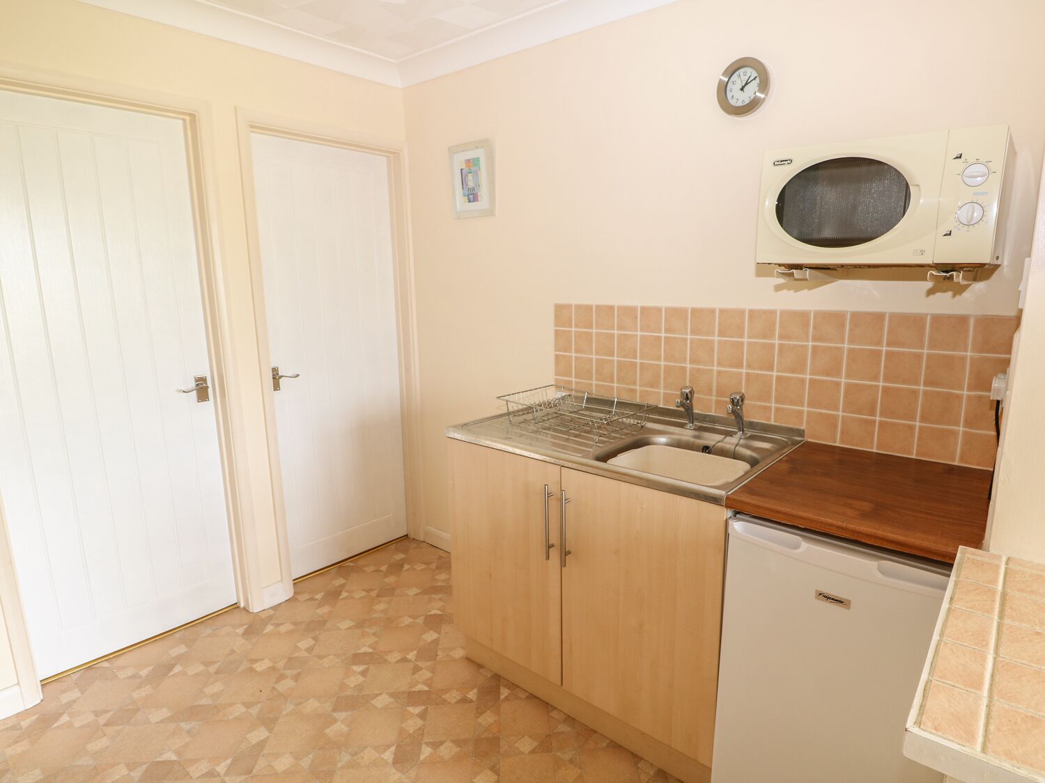 A small kitchen with a sink, a microwave, and a dishwasher. There is a door and a tiled backsplash.