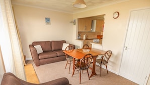 A compact living space with a brown sofa, a dining table with chairs, a kitchenette, and a white door. - Surf (Hunstanton)
