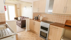 A compact kitchen with a stove, oven, and a microwave. There is a sink and a small refrigerator. The floor has a geometric tile pattern. - Surf (Hunstanton)