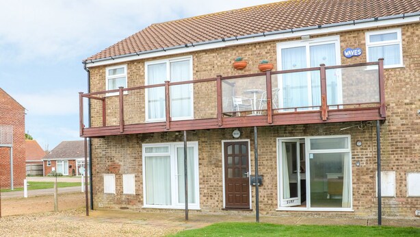 A two-story house with a balcony, a door labeled "WAVES", and a sign indicating a surf rental service. - Surf (Hunstanton)