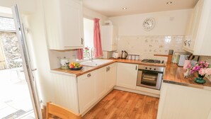 A kitchen with white cabinets, a wooden countertop, a sink, a stove, and a clock on the wall. - Herdwick Cottage (Grange-over-Sands)