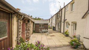 A courtyard with a stone table and chairs, surrounded by buildings with a mix of stone and plaster exteriors. - Herdwick Cottage (Grange-over-Sands)