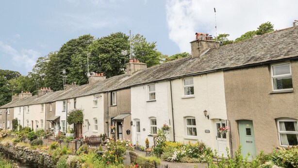 A row of traditional terraced houses with a stone wall and a small stream in the foreground. - Herdwick Cottage (Grange-over-Sands)