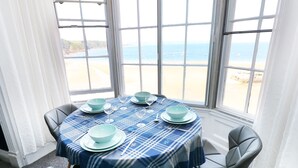 A dining table with a blue plaid tablecloth, four chairs, and a view of the beach through large windows. - Apartment 3 (Tenby)