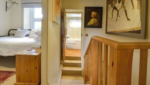 A bedroom with a bed, a wooden bench, a staircase, and a bathroom visible through an open door. - 11 The Village (Yelverton)