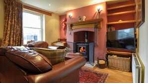 A cozy living room with a fireplace, leather sofa, and a television. - 11 The Village (Yelverton)