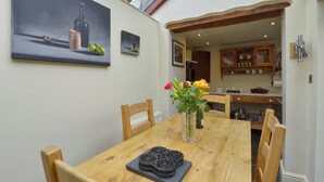 A dining area with a wooden table, chairs, a vase with flowers, and artwork on the wall. - 11 The Village (Yelverton)