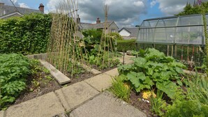 A garden with raised beds, a greenhouse, and a wooden trellis structure. - 11 The Village (Yelverton)