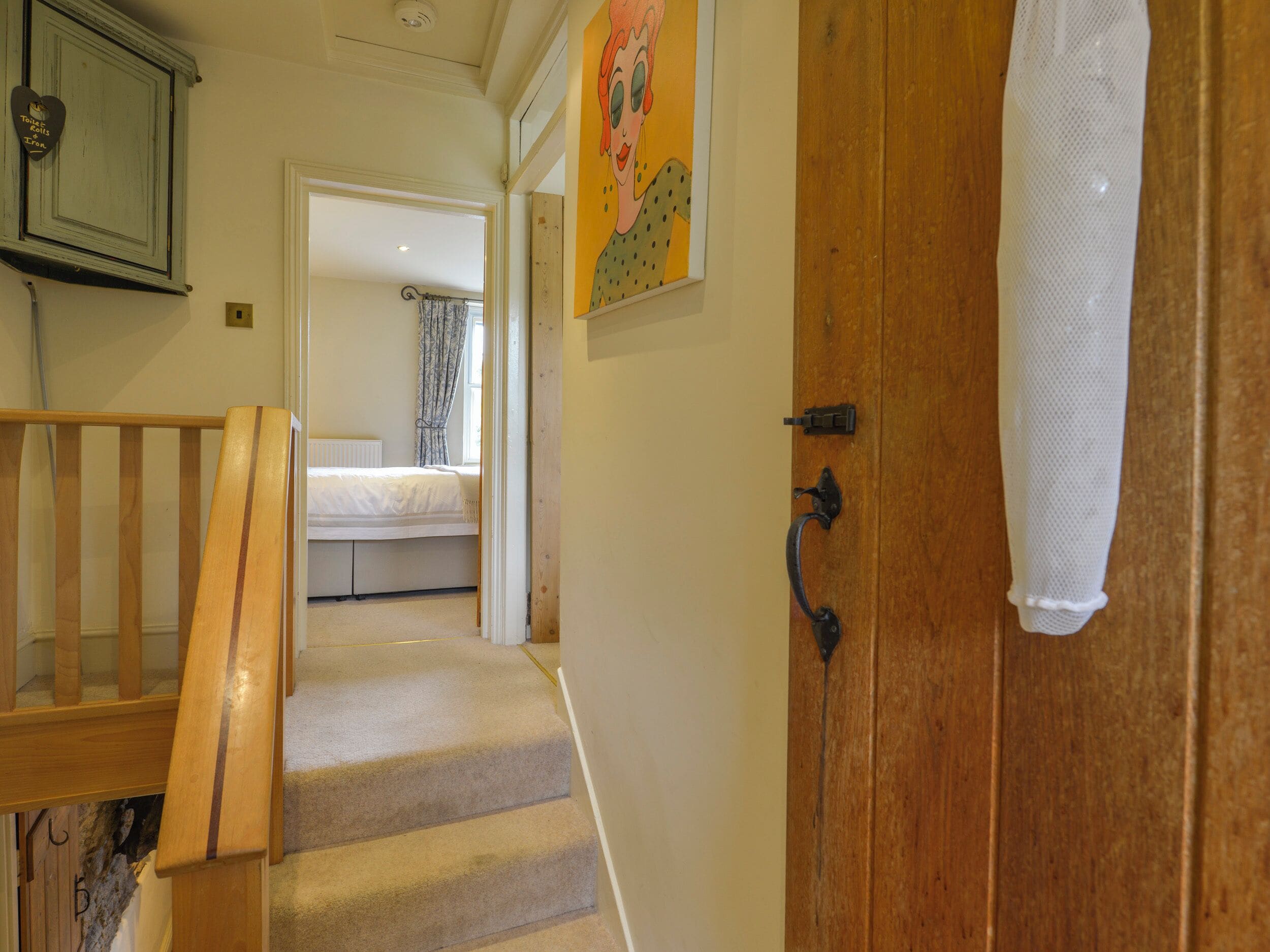 Una escalera que conduce a un dormitorio con una cama, una puerta de madera y un cuadro en la pared.