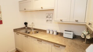 A kitchen with white cabinets, a double sink, a toaster, and a wall sign that says "Eat Drink & be Merry". - The Hen House (Thornton-Cleveleys)