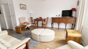 A living room with a sofa, ottoman, wooden coffee table, and a TV stand with a flat-screen TV. - The Hen House (Thornton-Cleveleys)